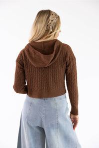 A woman shown from the back wearing a brown cable-knit cropped hoodie with a hood, paired with light blue jeans, against a plain white background.