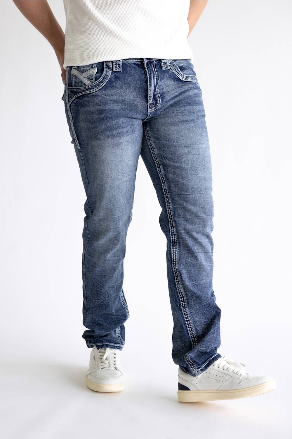 A person wearing medium-wash blue denim jeans with a white ribbed top and white sneakers, shown from the waist down against a plain light background.