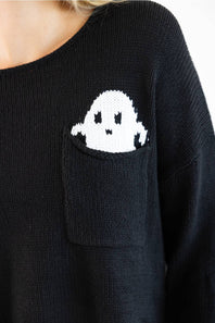 Close-up of a person wearing a black knit sweater with a white ghost motif knitted into the chest pocket.