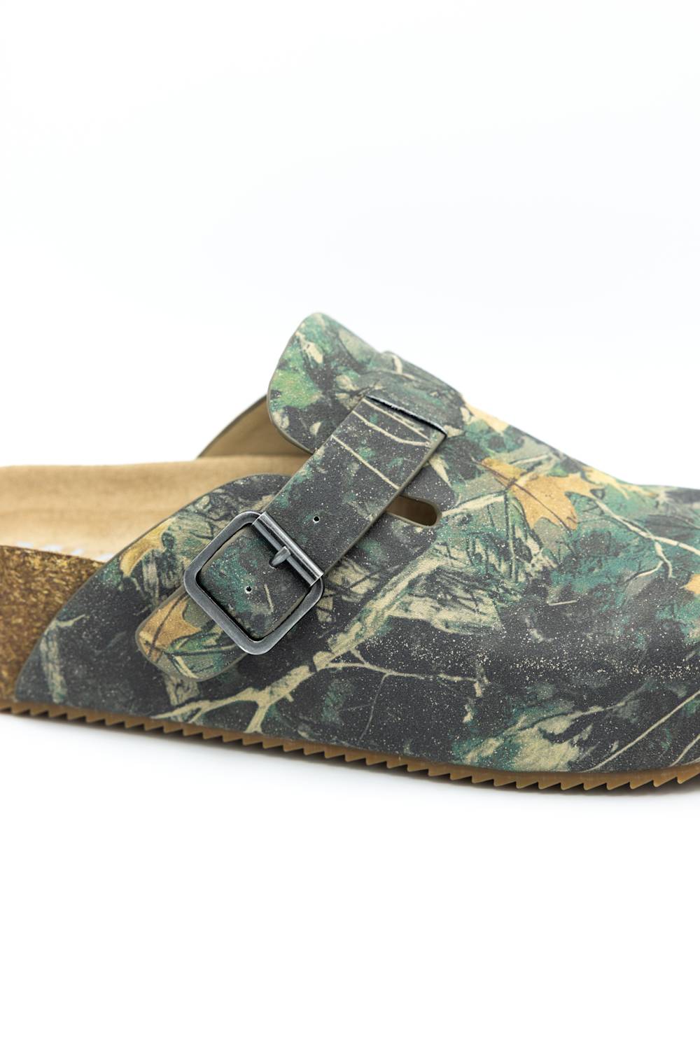 A close-up of a clog-style mule shoe with a woodland camouflage pattern in green, brown, and tan, featuring a dark gray double strap with a metal buckle and a cork-like midsole.