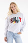 A woman wearing a light heather gray sweatshirt with a colorful 'HOLLY Jolly' graphic on the front, paired with light blue jeans.