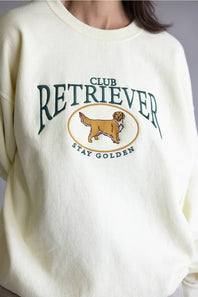 A close-up of a cream-colored crewneck sweatshirt featuring a green and gold graphic that reads 'CLUB RETRIEVER' and 'STAY GOLDEN' with an illustration of a golden retriever dog.