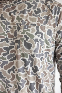 Close-up of a camouflage long-sleeve shirt with a chest pocket, featuring a pattern of beige, brown, green, and gray shapes.