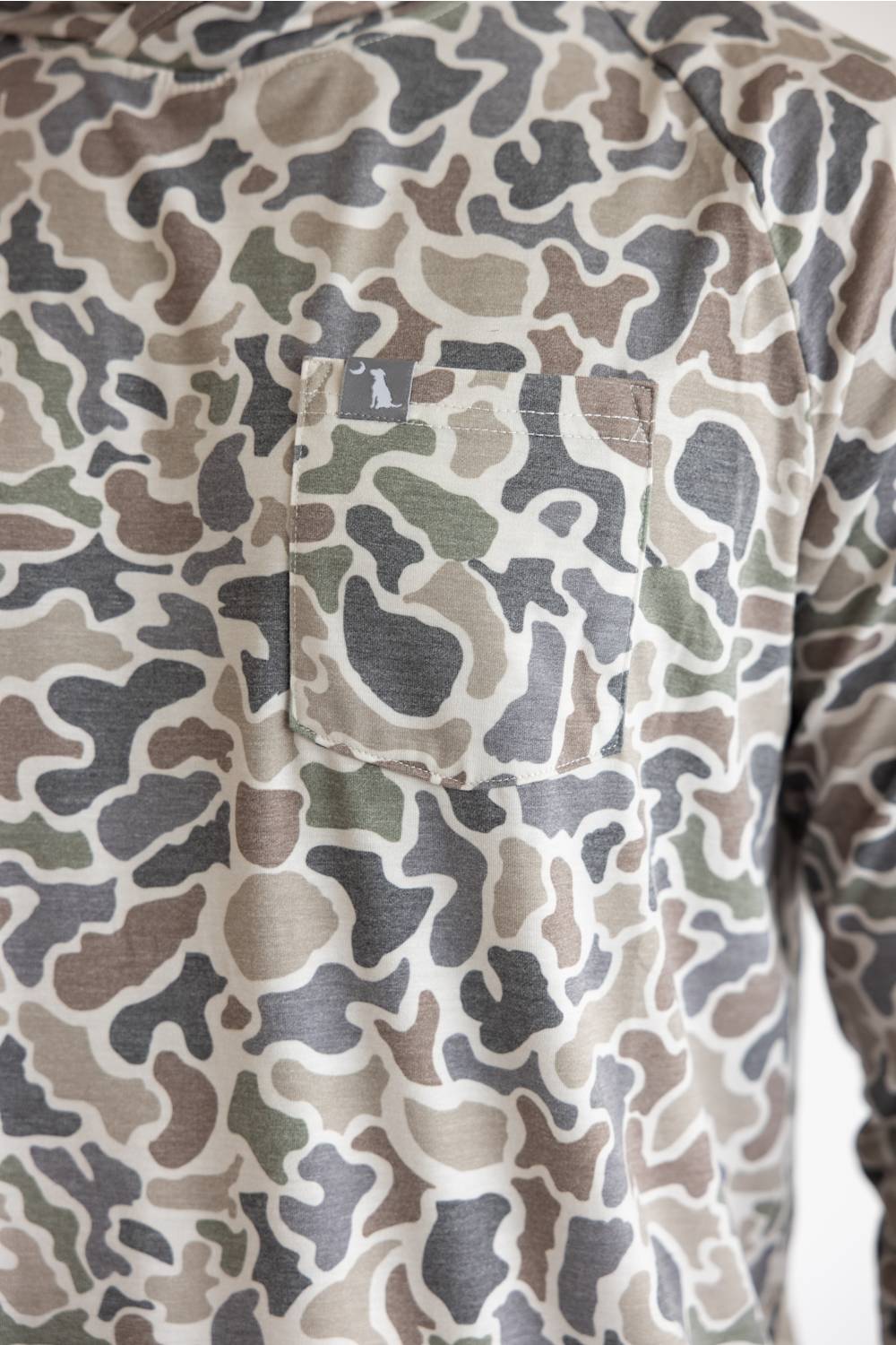 Close-up of a camouflage long-sleeve shirt with a chest pocket, featuring a pattern of beige, brown, green, and gray shapes.