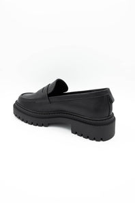 A single black leather penny loafer with a chunky lug sole, shown from a side-rear angle on a plain white background.
