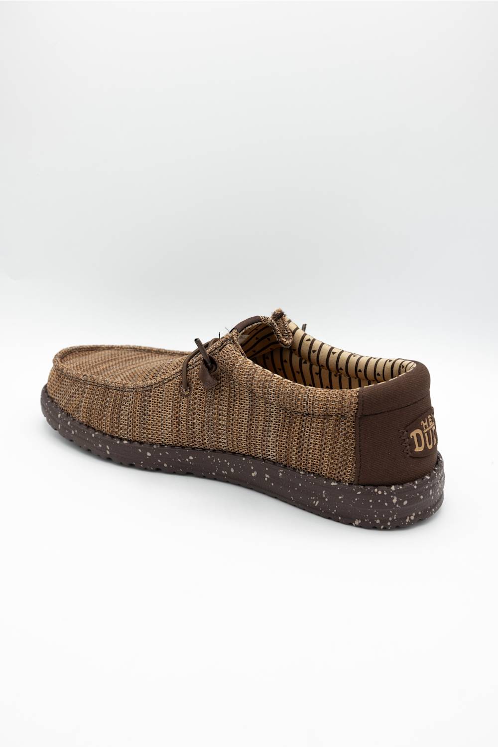 A single brown woven slip-on shoe with a textured knit upper, matching laces, and a speckled dark brown sole, shown against a plain light gray background.