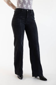 A person wearing black wide-leg cropped jeans with a high waist, paired with a patterned top and black pointed-toe heels, photographed against a plain white studio background.