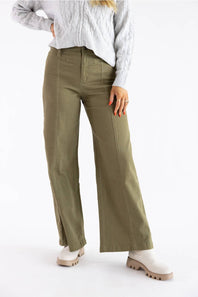 A model wearing olive green wide-leg pants, a light gray cable-knit sweater, and white boots, shown from the waist down against a white studio background.