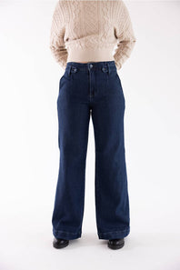 A person wearing dark blue wide-leg denim jeans and a beige cable-knit sweater, standing against a plain white studio background.