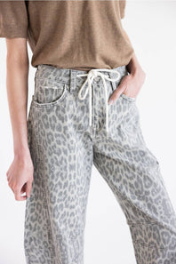 A person wearing light gray leopard-print jeans with a white drawstring waist, paired with a brown short-sleeve top, shown against a plain white background.