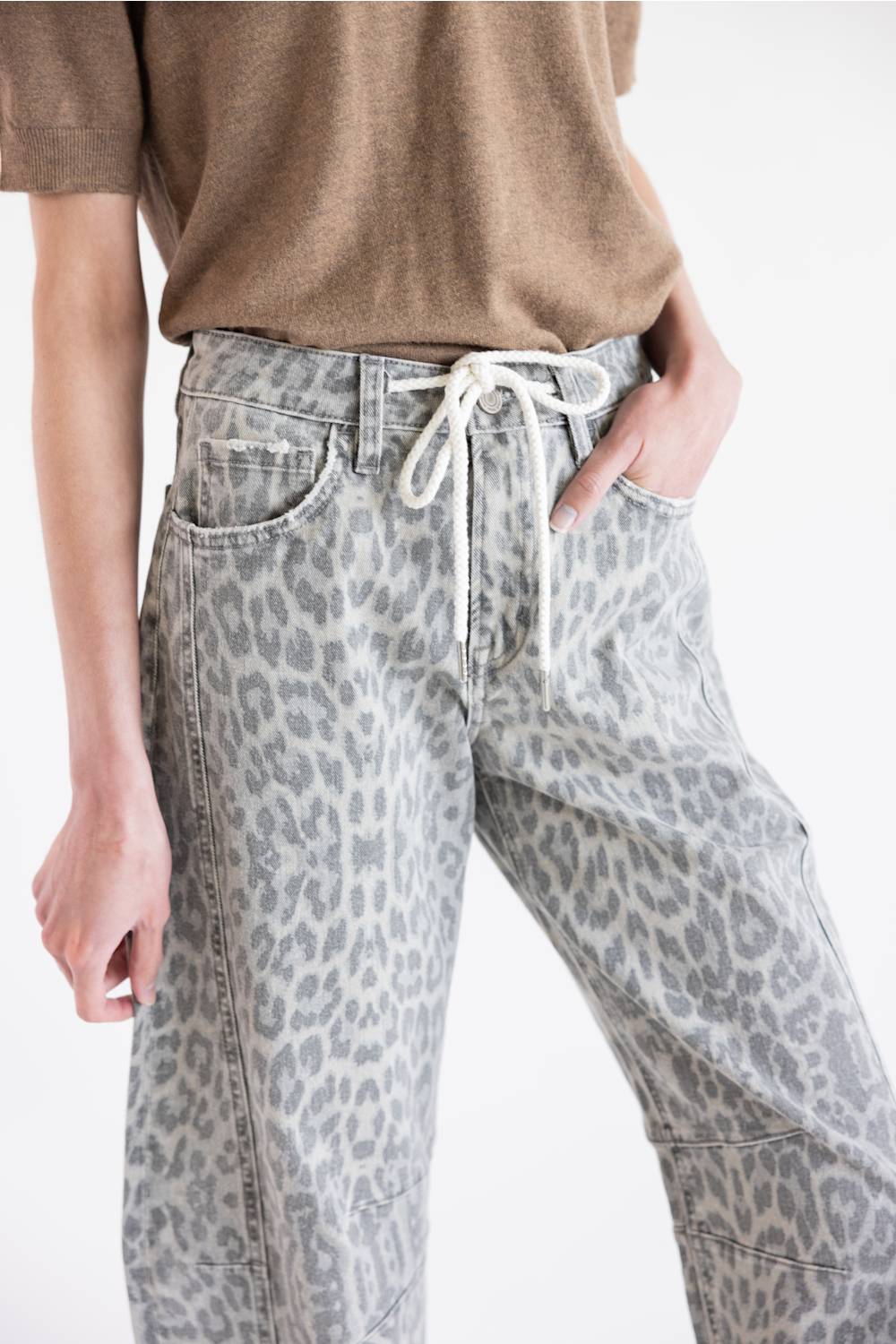 A person wearing light gray leopard-print jeans with a white drawstring waist, paired with a brown short-sleeve top, shown against a plain white background.