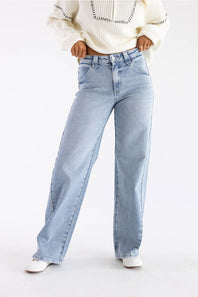 A person wearing light-wash wide-leg blue jeans, a cream knit sweater, and white pointed shoes, standing against a plain white studio background.