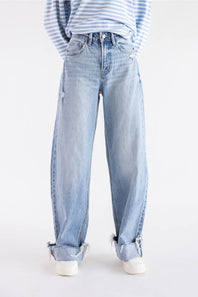 A person wearing light-wash blue wide-leg jeans with rolled cuffs, paired with a blue-and-white striped long-sleeve top and white sneakers, photographed against a plain white studio background.