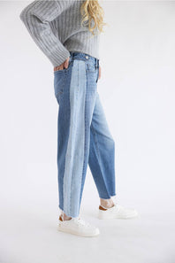 A model wearing light-wash wide-leg blue jeans, a gray ribbed knit sweater, and white sneakers, standing against a plain white studio background.