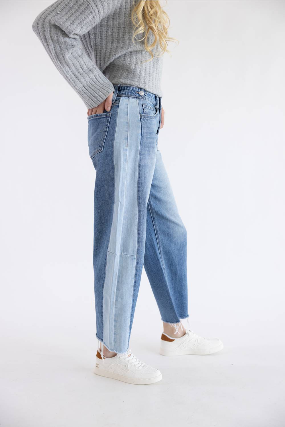 A model wearing light-wash wide-leg blue jeans, a gray ribbed knit sweater, and white sneakers, standing against a plain white studio background.
