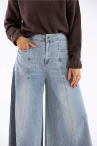 A person wearing light-wash wide-leg denim jeans and a dark brown knit sweater, shown from the chest down against a plain white studio background.