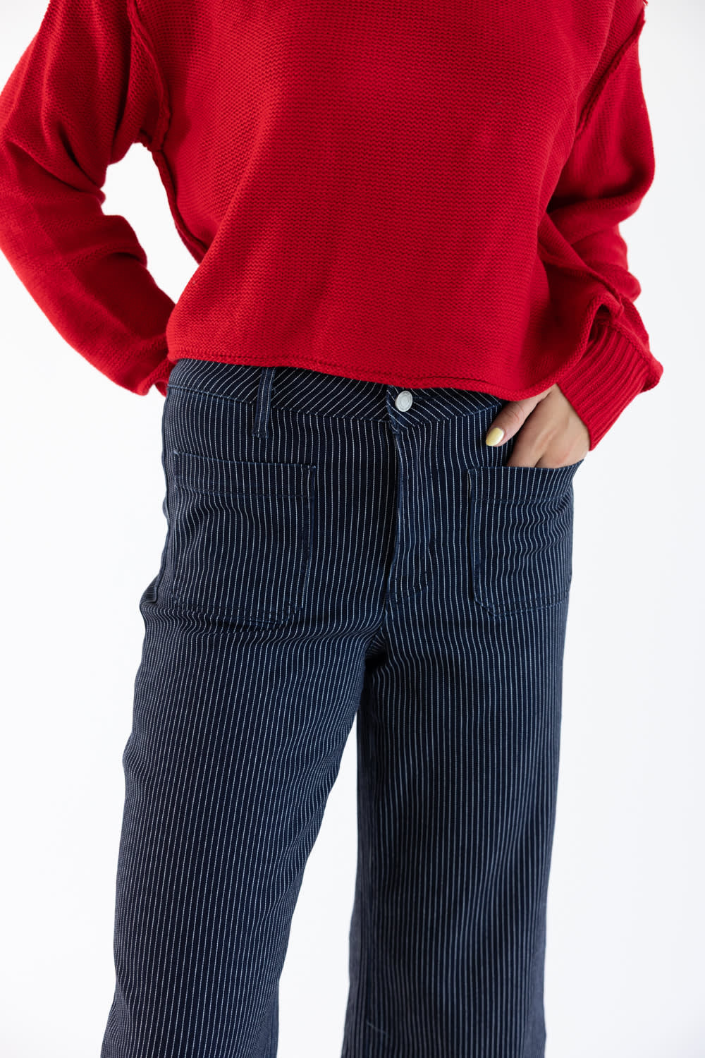 A person wearing a bright red ribbed knit sweater and navy corduroy pants, cropped from the chest down against a plain white background.
