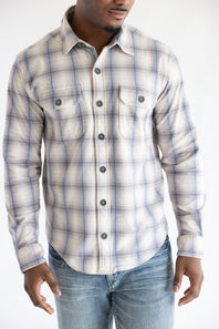 Cropped front-facing view of a man wearing the Hallstatt Knit Button Up Flannel Shirt in Sand with a blue, beige, and gray plaid pattern, paired with light-wash jeans.