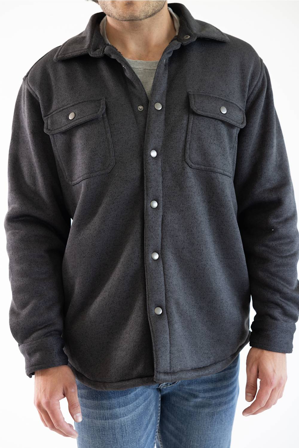 A man wearing a dark charcoal gray button-up flannel shirt jacket with two chest pockets and silver snap buttons, paired with blue jeans.