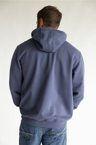 A man viewed from behind wearing a slate blue pullover hoodie and blue jeans, standing against a plain off-white background.
