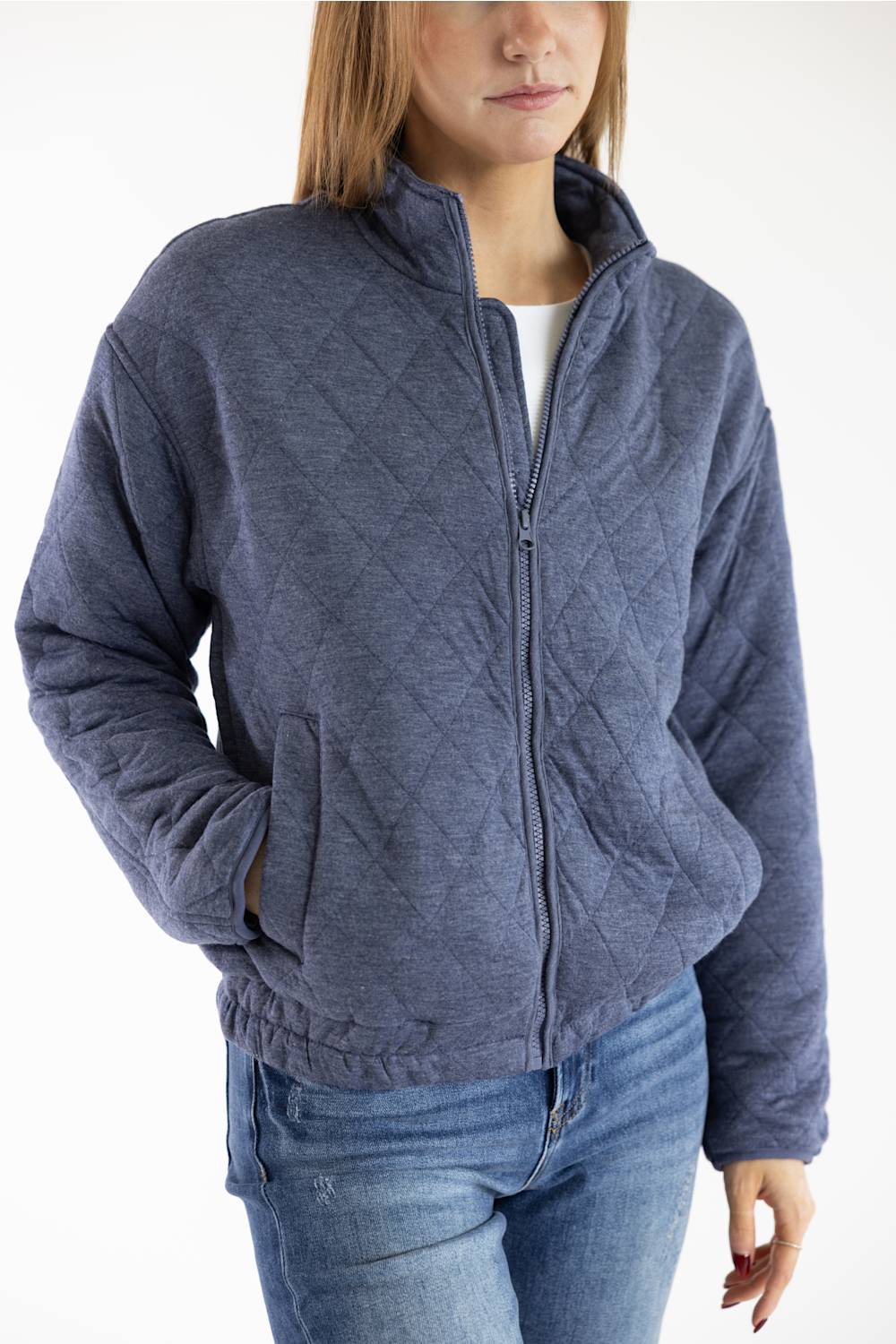 A woman wearing a heathered slate blue quilted zip-up jacket over a white top and blue jeans, shown from the waist up against a plain white background.