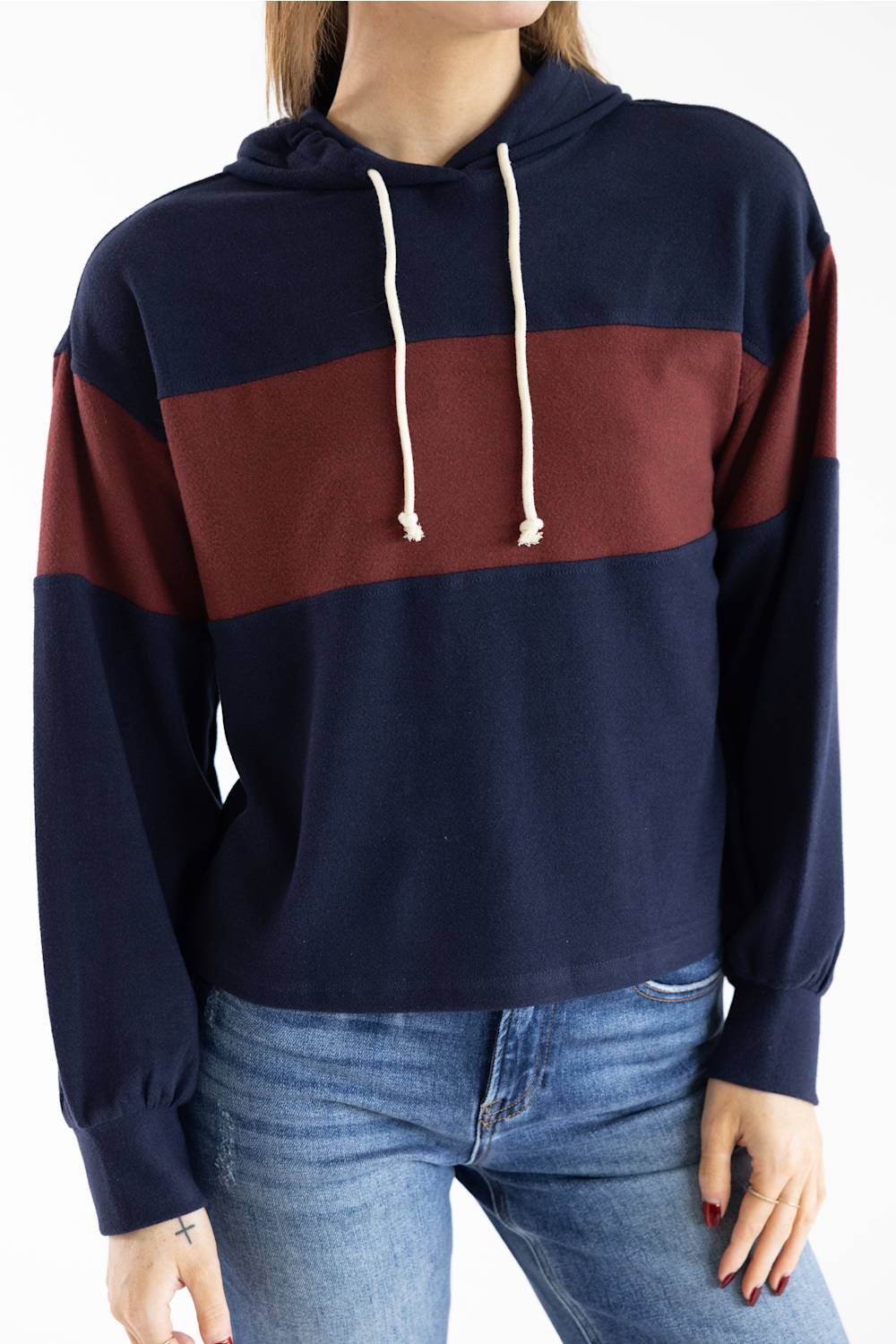 A woman wearing a cropped long-sleeve hoodie with horizontal navy blue and burgundy color-blocked stripes and cream drawstrings, paired with blue jeans.