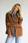 A woman wearing a brown corduroy utility jacket over a blue top and light wash jeans, posing against a light gray studio background.