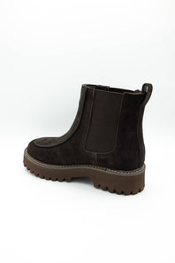 A dark brown suede Chelsea boot with a chunky lug sole, shown from a side-rear angle on a white background.