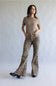 A woman modeling leopard-print flared pants and a beige short-sleeve top, standing against a neutral light gray studio backdrop.