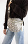 A person wearing a dark brown cardigan and light blue jeans carries a leopard-print crossbody bag with a beige strap and gold-tone hardware against a plain white background.