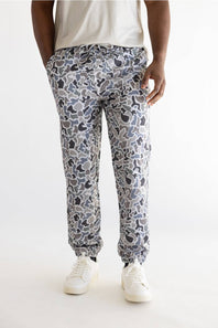 A person shown from the waist down wearing patterned jogger-style pants with a white t-shirt and white sneakers, photographed against a plain light background.