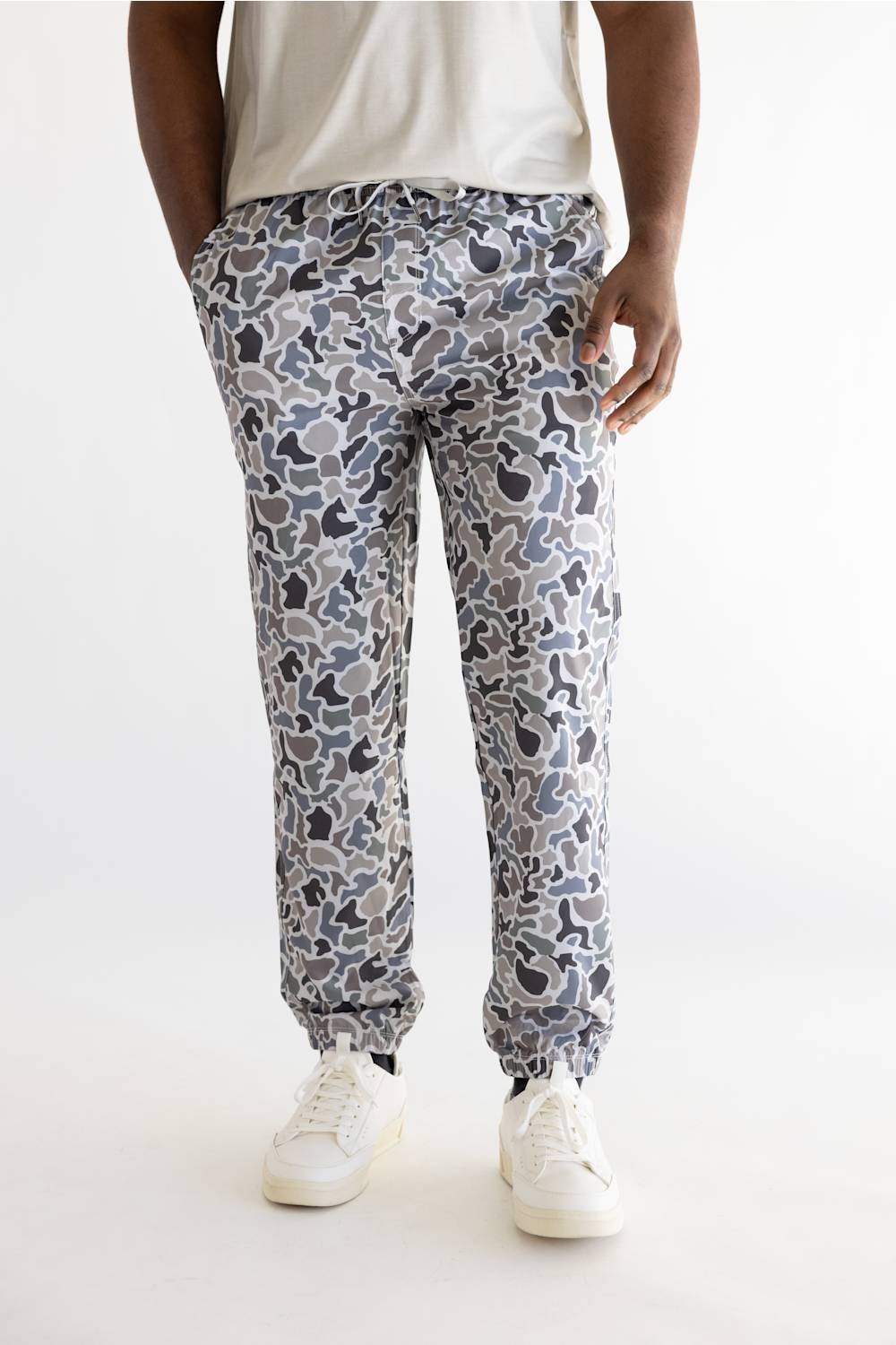 A person shown from the waist down wearing patterned jogger-style pants with a white t-shirt and white sneakers, photographed against a plain light background.