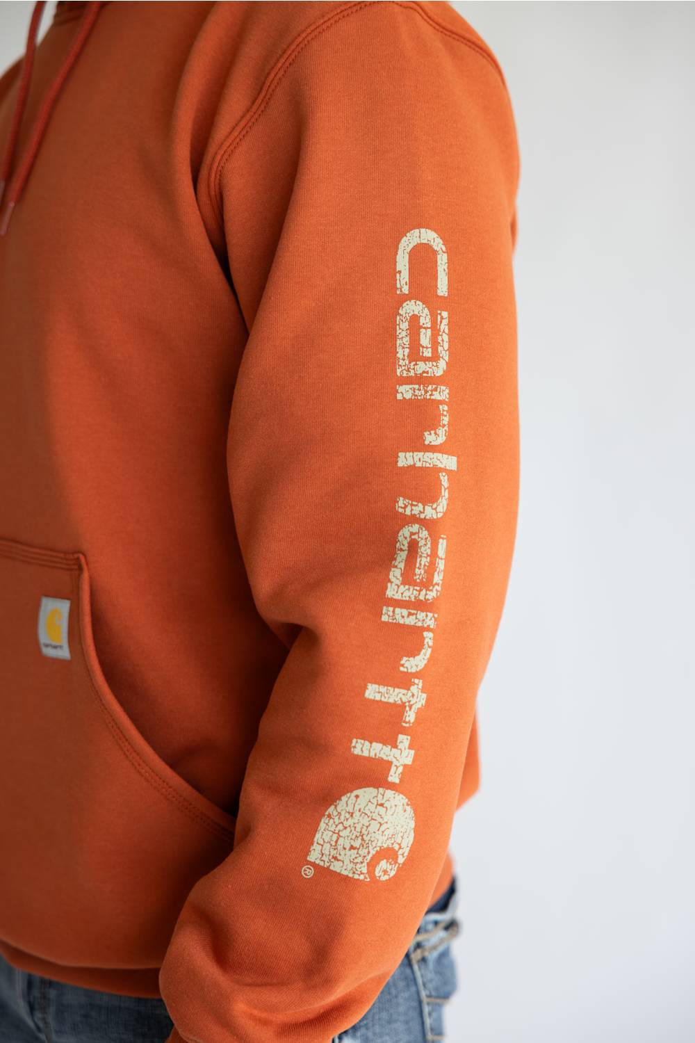 Man wearing a burnt orange colored hoodie, with Carhartt logo down the left arm sleeve. 