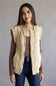 A woman modeling a sleeveless quilted vest in a warm cream-beige color, styled over a brown long-sleeve top and blue jeans against a plain gray studio background.
