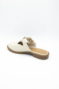 A single women's flat mule sandal in off-white leather with a cutout toe, a decorative strap with a gold-tone buckle, and a brown sole, shown from a side-rear angle on a white background.