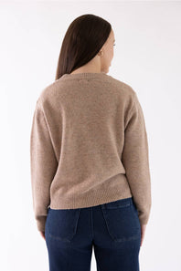 A woman viewed from the back wearing a light brown knit sweater and dark blue jeans against a plain white background.