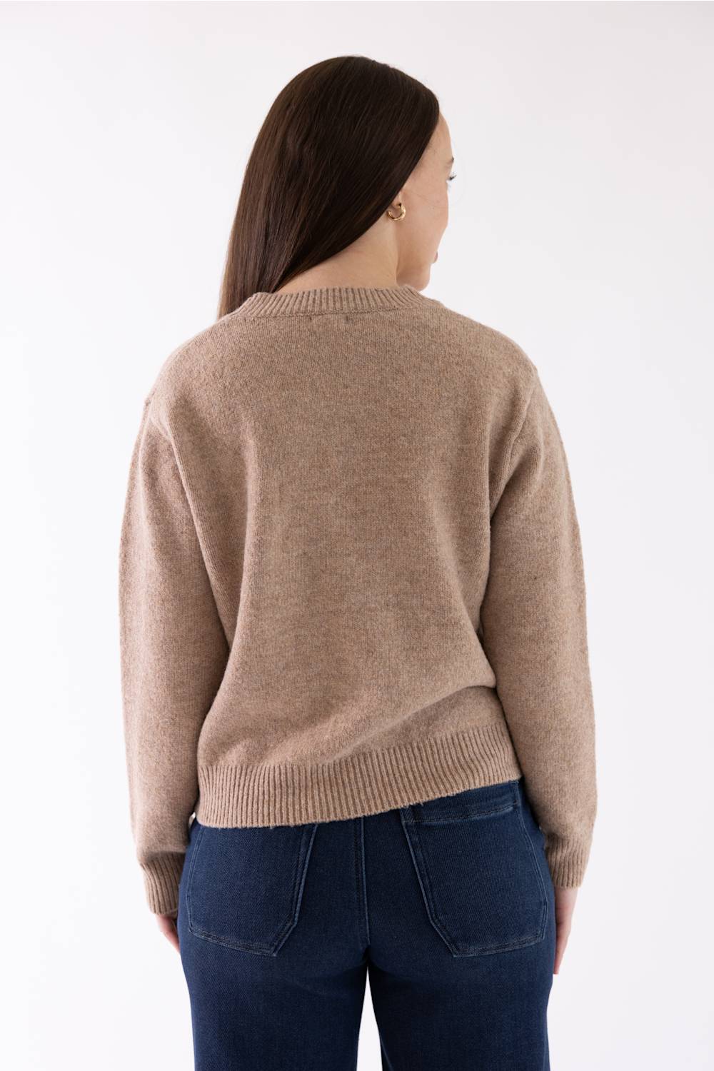 A woman viewed from the back wearing a light brown knit sweater and dark blue jeans against a plain white background.