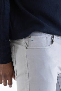 Close-up of a person wearing light gray slim-fit jeans and a dark navy ribbed sweater, showing the back pocket and waistband details.