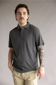 Kuhl De Facto Polo Shirt for Men in Carbon; Man wearing a dark gray polo shirt and beige pants against a plain background