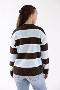 A woman shown from the back wearing a knit sweater with horizontal stripes in dark brown, light blue, and off-white, paired with light-wash jeans against a plain white studio background.