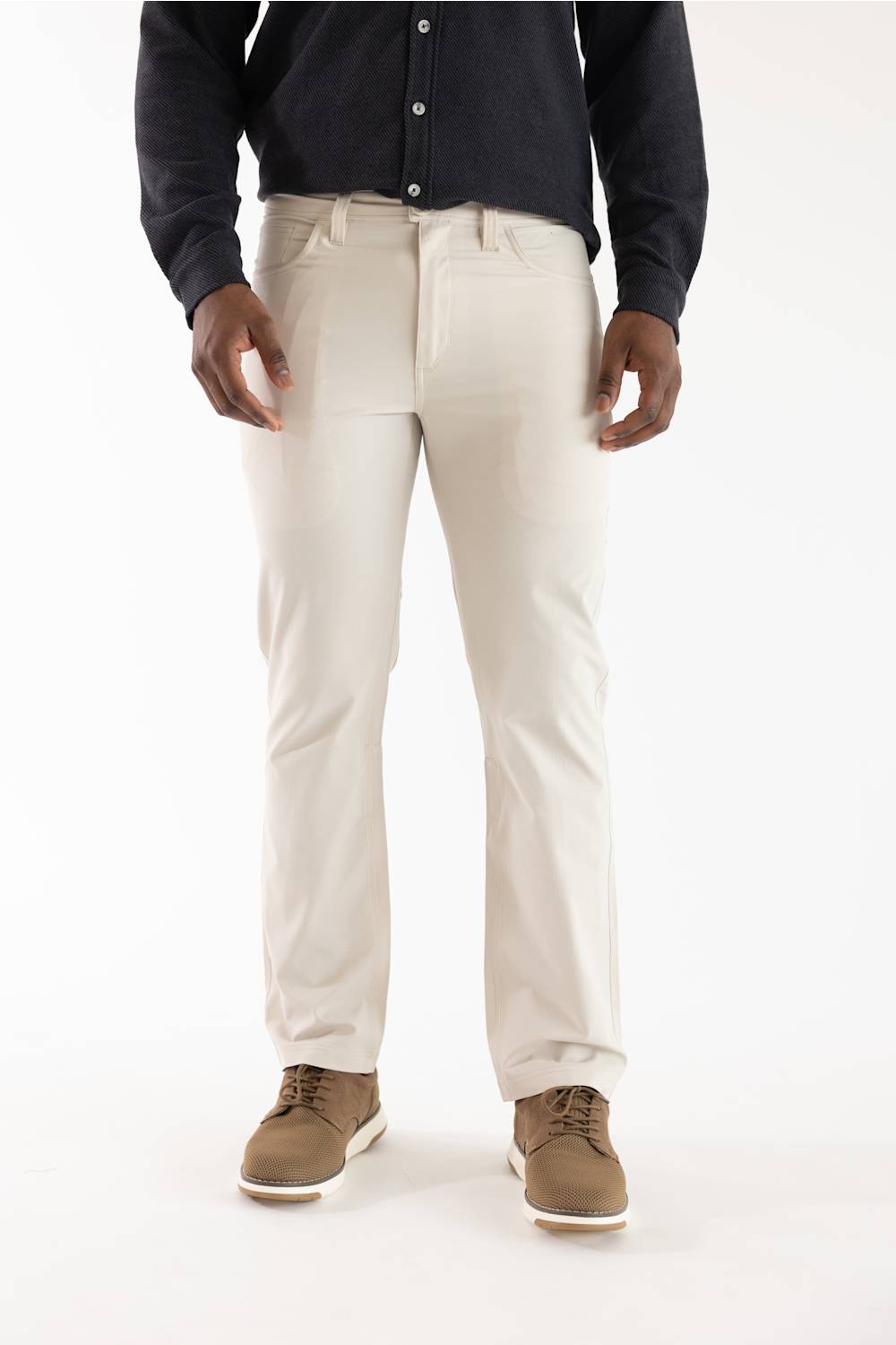 A person wearing light beige straight-leg dress pants, a dark navy long-sleeve button-up shirt, and brown suede shoes, shown from the waist down against a plain white studio background.