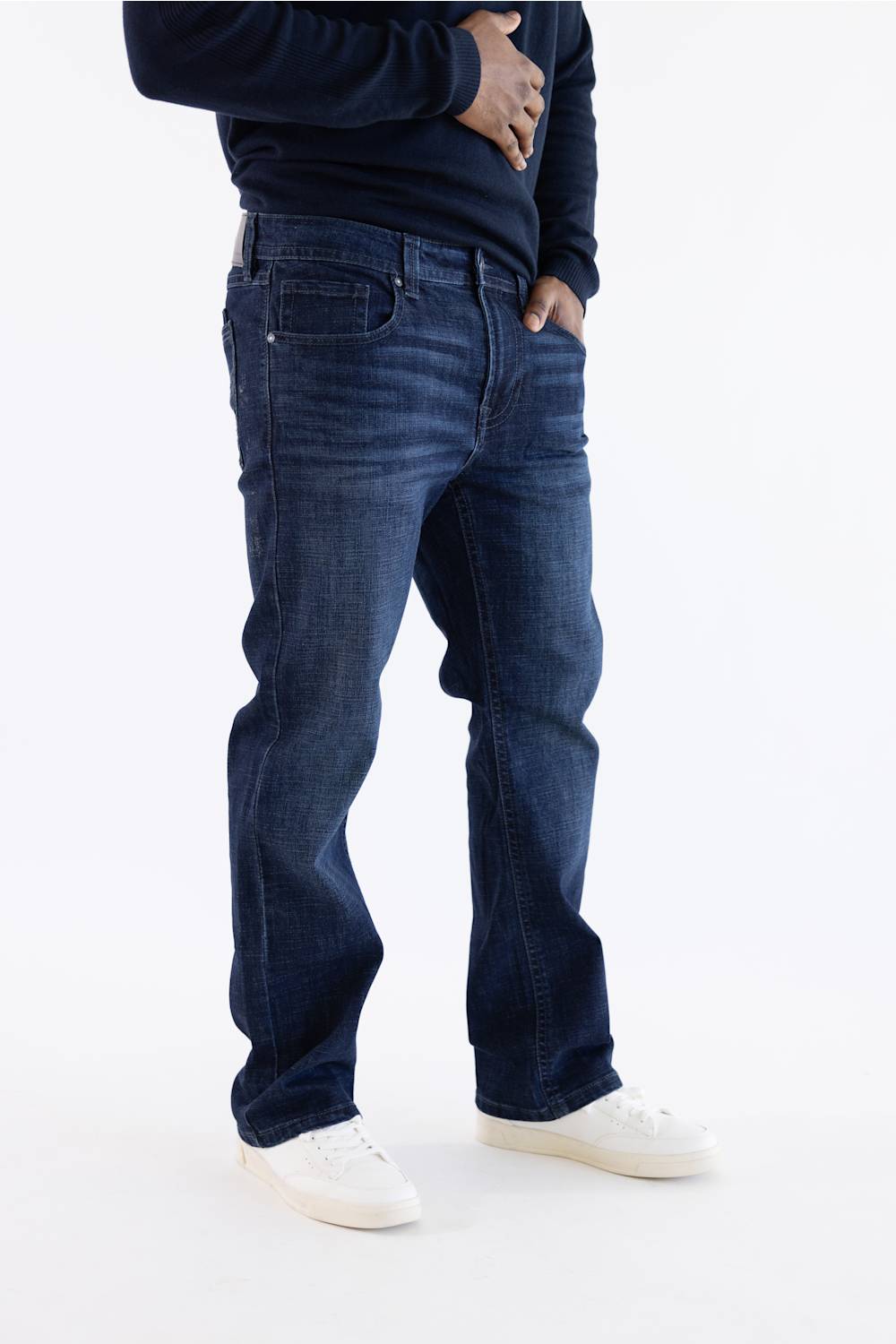 A person wearing dark blue straight-leg jeans, a navy long-sleeve top, and white sneakers, shown from the chest down against a plain white studio background.