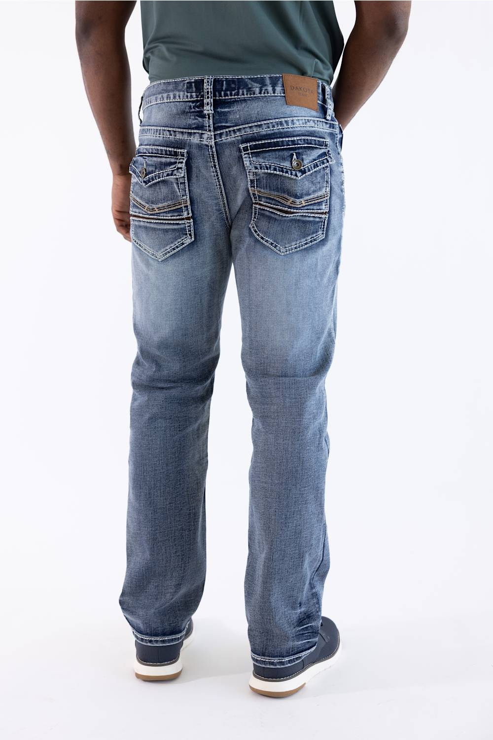 Rear view of a person wearing blue denim jeans with a faded wash, dark green shirt, and dark sneakers against a plain white background.