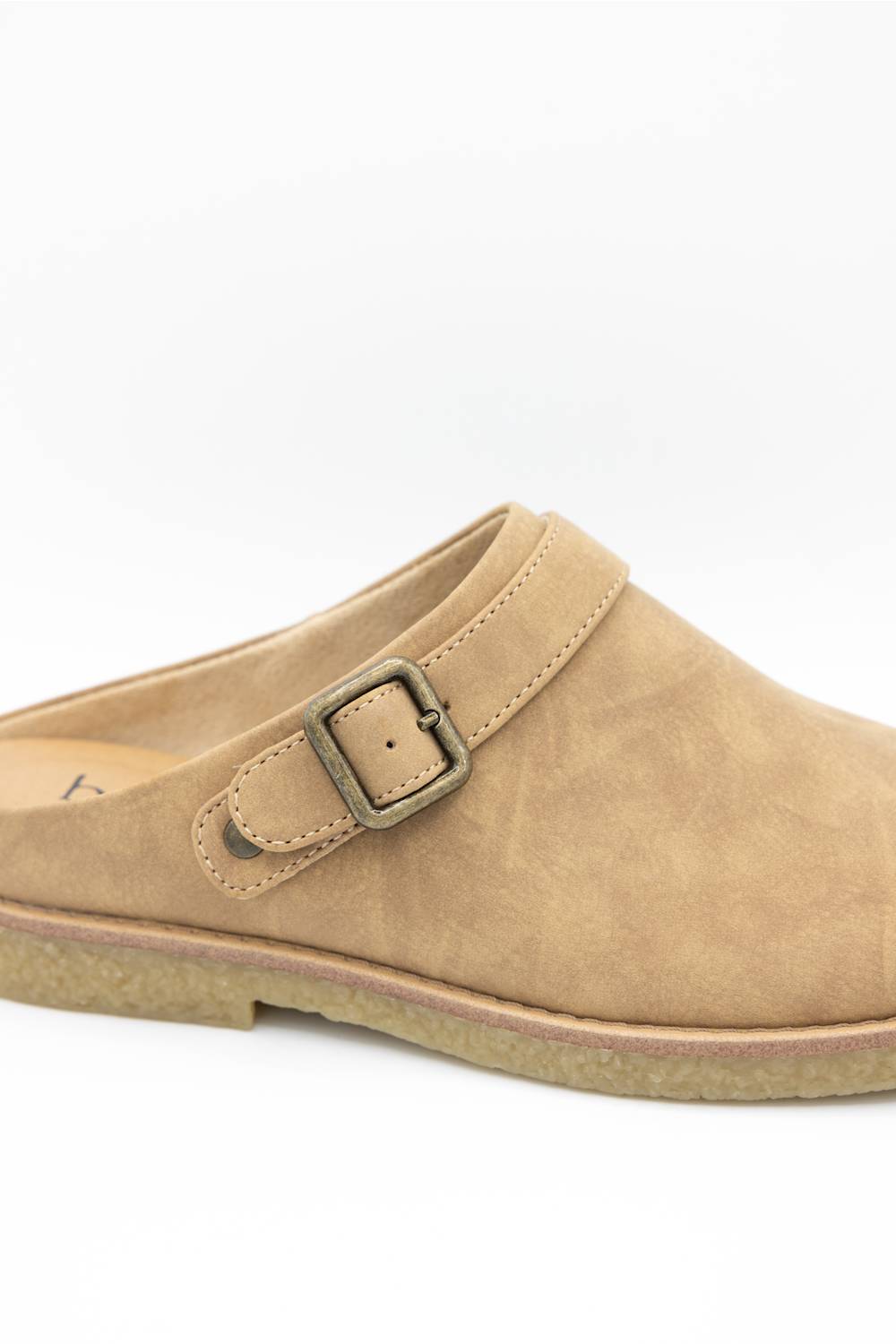 A light tan suede clog-style mule shoe with a single strap and an antique bronze buckle, shown from a side angle on a white background.