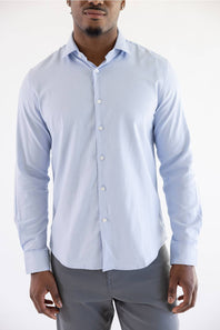 A man wearing a light blue long-sleeve button-down dress shirt with grey trousers, shown from the chin down against a plain white studio background.