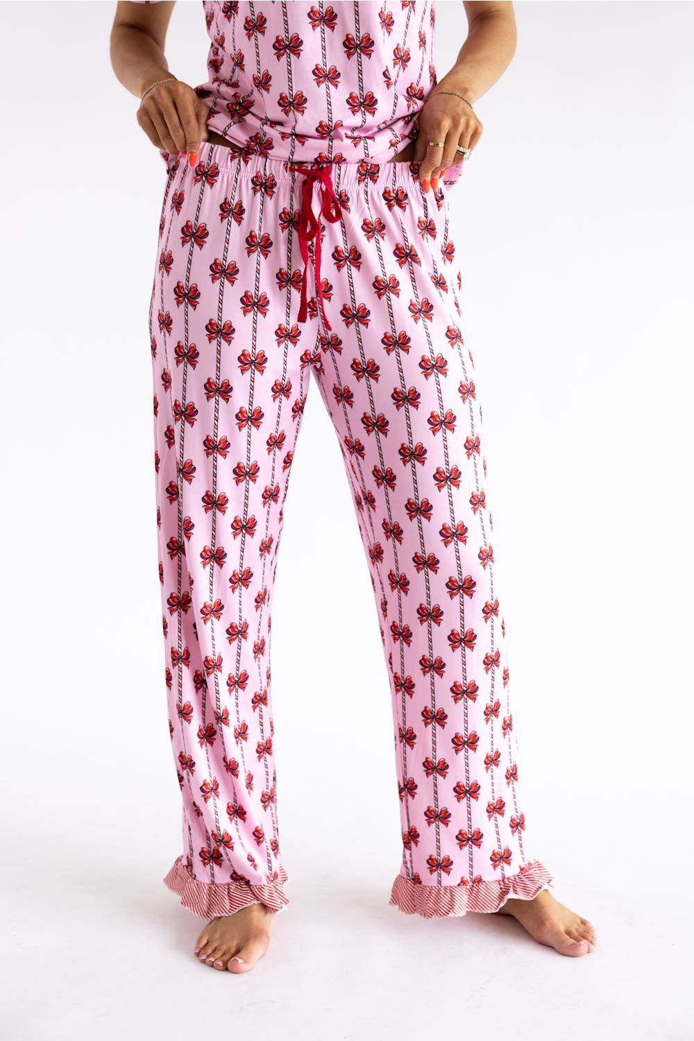Pink pajama pants with a red bow pattern, featuring a red drawstring waist and ruffled cuffs, shown on a model against a white background.