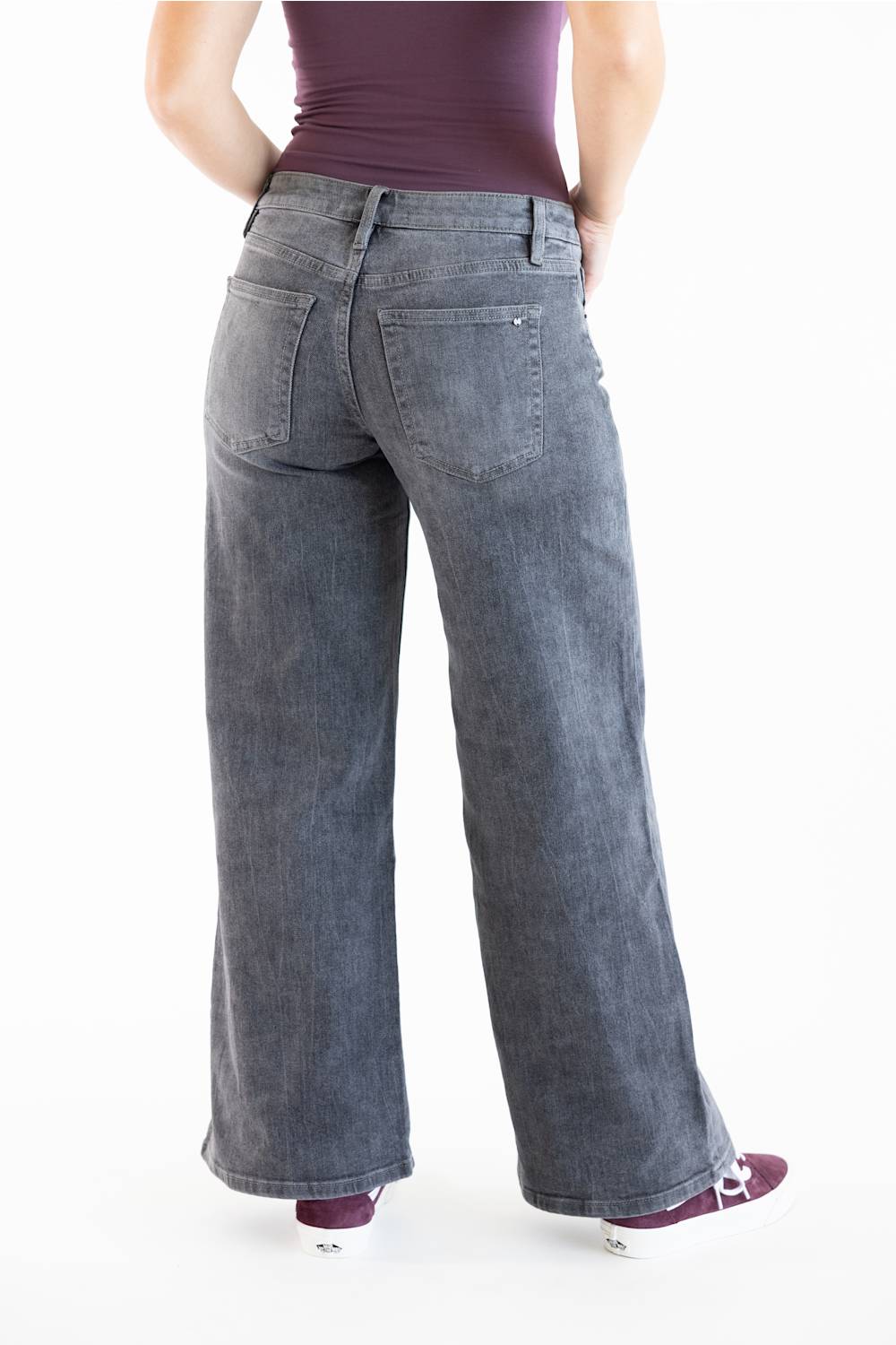 A person shown from the back wearing wide-leg gray denim jeans, a dark purple top, and purple sneakers against a plain white studio background.