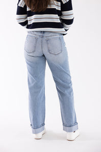 A person shown from the back wearing light-wash blue jeans, a navy, white, and gray striped long-sleeve top, and white sneakers against a plain white studio background.