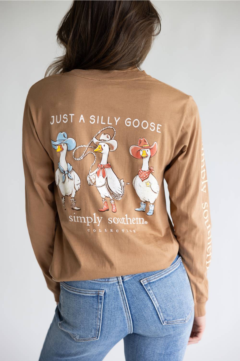 A brown long-sleeve t-shirt with a graphic of three western-style geese on the back, featuring the text 'JUST A SILLY GOOSE' and 'simply southern.' on the back, and 'simply southern.