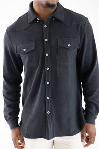 A man wearing a dark charcoal gray textured long-sleeve western shirt with silver buttons and two chest pockets, paired with white pants.